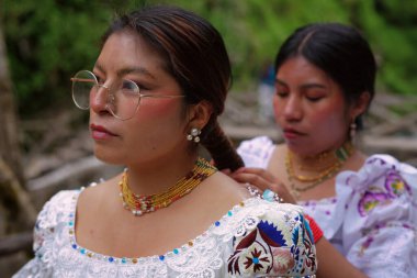 Geleneksel beyaz işlemeli bluz ve altın mücevher giyen iki yerli otavalo kadın, And Dağları 'ndaki Ekvador' da yerel bir kutlamaya hazırlanıyor.