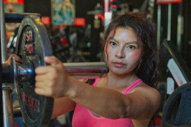 Genç İspanyol sporcu halterlere ağırlık ekliyor, spor salonunda yoğun bir antrenman için hazırlanıyor, kararlılığını gösteriyor ve fitness hedeflerine ulaşmaya odaklanıyor.