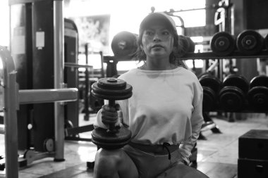 Konsantre sporcu kadın, modern spor salonunda ağırlık kaldırırken ve biceps egzersizleri yaparken halterleri kaldırıyor.