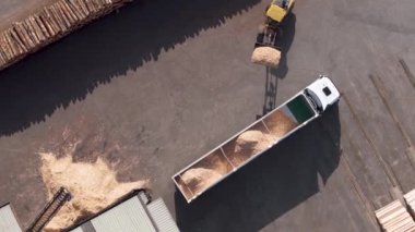 Yükleyici, kereste fabrikasındaki karavan kamyonuna talaş yüklüyor. Havadan aşağı, dönen atış
