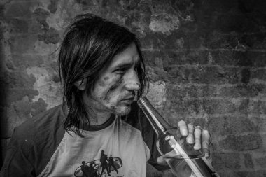 Eski tuğla duvarın yanında bir şişe alkollü siyah saçlı adam.