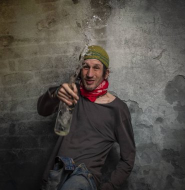 Yaşlı taş duvarın yanında votka şişesi olan pis alkolik bir erkek.