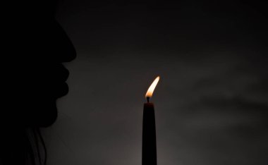 Silhouette of male with light of thin candle with dark background