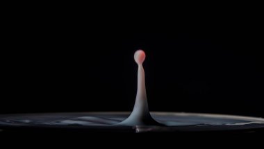 Color fresh sweet milk drops into another color of milk in cup with dark background