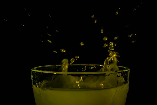 Color fresh yellow milk drops into white milk in cup with dark black background