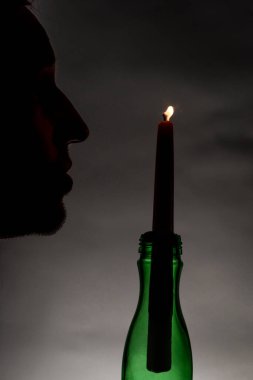 Silhouette of male with light of thin candle with dark background