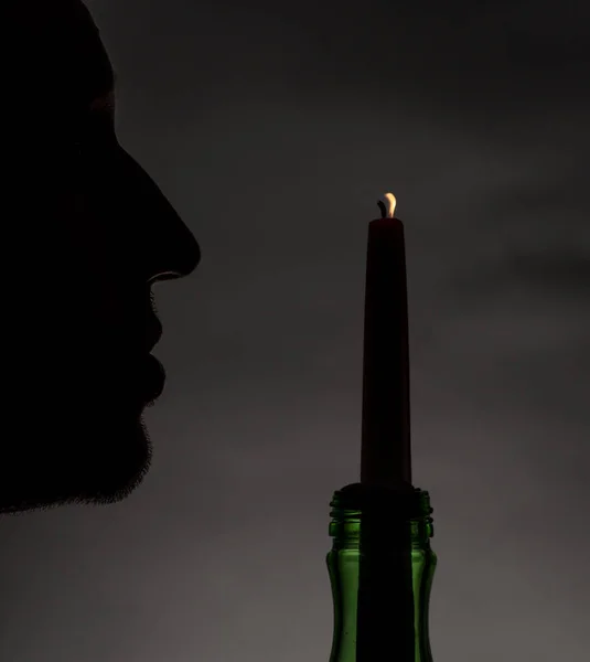 Silhouette of male with light of thin candle with dark background