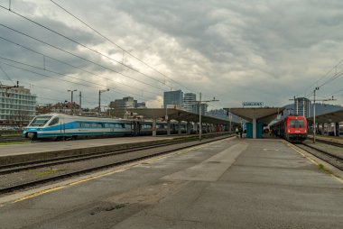 Yolcu trenleri bulutlu bahar mevsiminde başkenti Ljubljana 'da karanlık bir günde istasyonda.