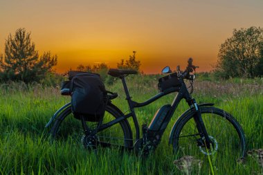 Güneş battıktan sonra turuncu gökyüzü olan siyah çantalı elektrikli bisiklet.