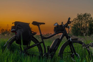 Güneş battıktan sonra turuncu gökyüzü olan siyah çantalı elektrikli bisiklet.