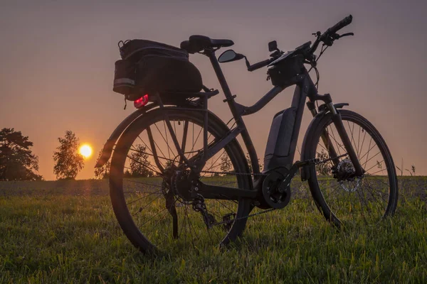 stock image Electric bike with black bag on meadow near Budweis with after sunset orange sky