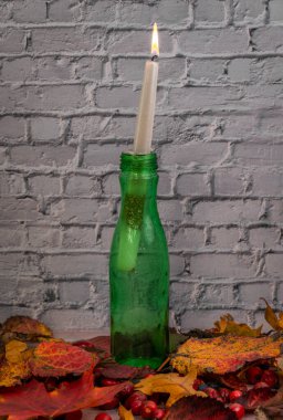 Yeşil şişe ve mum beyaz tuğla duvar sonbahar ağaç yaprakları