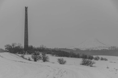 Beyaz fırtınada Rana tepesi. Eski harabe bacası olan Louny kasabası yakınlarında karlı bir sabah.
