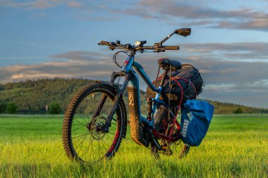 Güneş batarken yol kenarında elektrikli bisiklet ve Kremze CZ 06 14 2024 yakınlarında taze çayır.