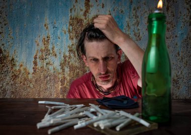 Siyah saçlı, esrarkeş beyaz adam. Bardaklar dolusu alkol ve renkli metalik duvar arkaplanı.