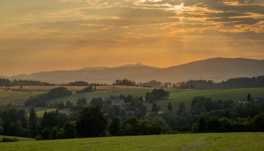 Yazın gün batımı Krkonose dağlarında sıcak tahıl tarlası ve yeşil çayır.