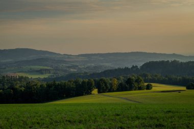 Yazın gün batımı Krkonose dağlarında sıcak tahıl tarlası ve yeşil çayır.