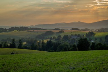 Yazın gün batımı Krkonose dağlarında sıcak tahıl tarlası ve yeşil çayır.