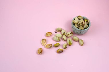 Pembe arka planda kase ile izole edilmiş tuzlu fıstıklı yakın plan.