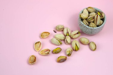 Pembe arka planda kase ile izole edilmiş tuzlu fıstıklı yakın plan.