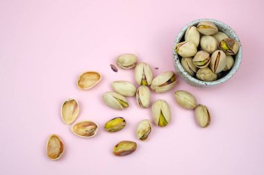 Pembe arka planda kase ile izole edilmiş tuzlu fıstıklı yakın plan.