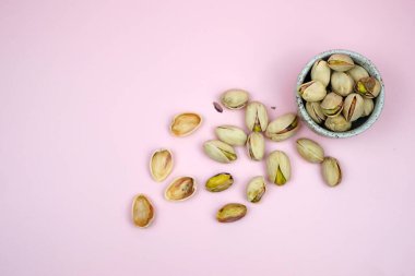 Pembe arka planda kase ile izole edilmiş tuzlu fıstıklı yakın plan.