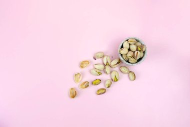 Pembe arka planda kase ile izole edilmiş tuzlu fıstıklı yakın plan.