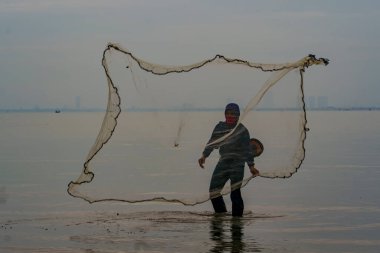 1 Ocak 2023. Balıkçı Endonezya Madura 'da balık ağı kullanarak sahilde balık yakalıyor..
