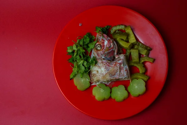 Steamed red snapper head with bitter gourds and chayotes on red plate. Studio shot. Selective focus. Copy space.