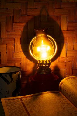 Kutsal Kur 'an, geleneksel gazyağı lambası ve arka planında örülmüş bambu olan ahşap masanın üzerinde. Stüdyo uzun pozlu. Odaklanmamış.