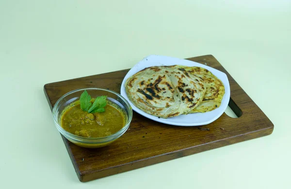 stock image roti canai and curry sauce in white plate with served on the wooden chopping board. Isolated on white.