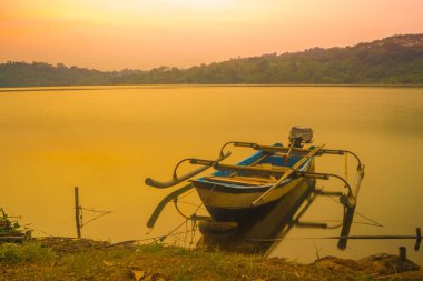 Geleneksel tekne Jatibarang Barajı, Semarang, Endonezya 'da gündoğumu sırasında sakin ve sakin göle demirledi. Uzun pozlu fotoğrafçılık.