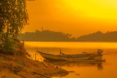Geleneksel tekne Jatibarang Barajı, Semarang, Endonezya 'da gündoğumu sırasında sakin ve sakin göle demirledi. Uzun pozlu fotoğrafçılık.