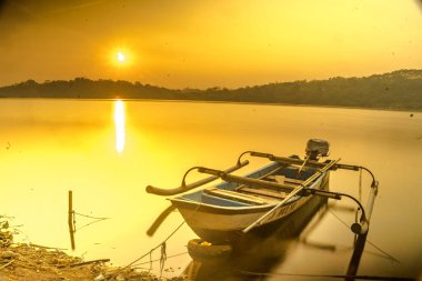 Geleneksel tekne Jatibarang Barajı, Semarang, Endonezya 'da gündoğumu sırasında sakin ve sakin göle demirledi. Uzun pozlu fotoğrafçılık.