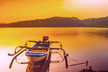 Geleneksel tekne Jatibarang Barajı, Semarang, Endonezya 'da gündoğumu sırasında sakin ve sakin göle demirledi. Uzun pozlu fotoğrafçılık.