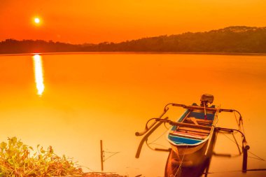 Geleneksel tekne Jatibarang Barajı, Semarang, Endonezya 'da gündoğumu sırasında sakin ve sakin göle demirledi. Uzun pozlu fotoğrafçılık.