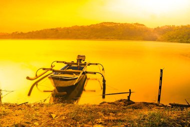Geleneksel tekne Jatibarang Barajı, Semarang, Endonezya 'da gündoğumu sırasında sakin ve sakin göle demirledi. Uzun pozlu fotoğrafçılık.