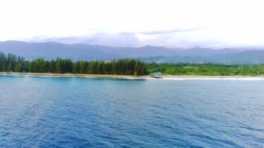 Blangpidie, Güneybatı Aceh, Endonezya 'daki güzel Bali Sahili' nde mavi okyanusla hava aracıyla mavi gökyüzü vuruşu. Gökyüzüne karşı kumlu sahilde yeşil çam ağaçları.