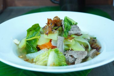 Muz yaprağıyla kaplanmış, beyaz bir tabakta servis edilen, Çin lahanası ve romaine marullu kızarmış biftek..