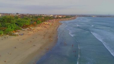 Kalabalık bir günde Legian Beach, Kuta, Bali 'nin hareketli atmosferi, ağaçların ve otellerin manzarası, İHA kullanarak havadan çekildi. Hava Videosu.