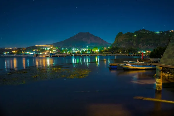 Batur Gölü, Kintamani, Bali 'deki akşam atmosferi, Batur Dağı' nın yansıması ve göl kenarındaki köyün atmosferi parlak ışıklarla aydınlatılıyor. Gece Fotoğrafçılığı.