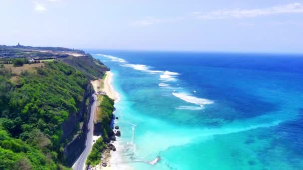 空から見ると バリのパンダワビーチは 透明な青い水 白い砂 沿岸の岩 道路の崖で育つ緑豊かな植生を誇っています ドローンで撮影した航空写真 — ストック動画