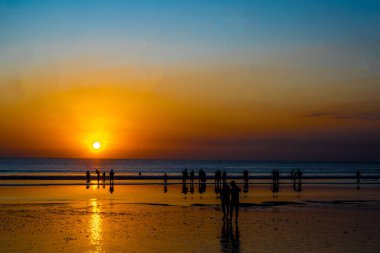 Bali 'deki Kuta Sahili' nde gün batımının tadını çıkaran insanların silueti. Sokak Fotoğrafçılığı