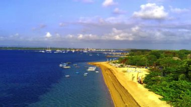 Sanur, Bali 'deki Cemara Sahili' nin güzelliği, havadan çekildi. Kremsi kum, masmavi deniz, yemyeşil ağaçlar ve sahile demir atmış birkaç tekne. Hava görüntüleri.