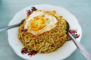 Kaşık ve çatalla servis edilen bir tabakta servis edilen, güneşli bir tarafı olan sarı hazır erişte tabağı..