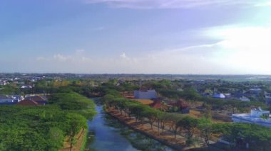 Endonezya, Surabaya 'da bir ırmağın üzerinde bir dron süzülüyor. Nehir yemyeşil ağaçlarla çevrili ve gökyüzü açık mavi. Drone kamerası sahnenin güzelliğini yakalar.