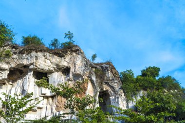 Ağaçlarla süslenmiş yıpranmış bir kireçtaşı kayalığı Setigi, Gresik, Doğu Java, Endonezya 'da açık mavi bir gökyüzüne karşı dimdik ayakta duruyor. Doğa ve manzara fotoğrafçılığı.