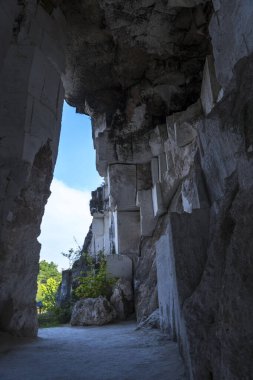 Koyu, yosunlu, kireçtaşı bir mağarada dikdörtgen şeklinde bir açıklık, tüylü beyaz bulutlarla dolu parlak mavi bir gökyüzünü çerçeveler. Seyahat Fotoğrafçılığı.