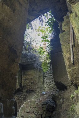 Koyu, yosunlu, kireçtaşı bir mağarada dikdörtgen şeklinde bir açıklık, tüylü beyaz bulutlarla dolu parlak mavi bir gökyüzünü çerçeveler. Seyahat Fotoğrafçılığı.