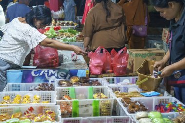 24 Kasım 2023. Surabaya, Endonezya. Pasar Kue Subuh ya da pazar yerinde şafak vakti abur cubur satılıyor. Kalabalık bir pazar yerinde insanlar renkli tezgahların etrafında toplanmış çeşitli abur cuburlarla dolup taşıyor. Sokak Editörü Fotoğrafçılık.